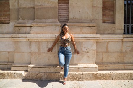 Téléchargez les photos : Belle jeune femme blonde espagnole se penche contre le mur d'un vieux bâtiment à Séville. La femme est habillée en jeans. La femme fait du tourisme et visite l'Espagne. - en image libre de droit
