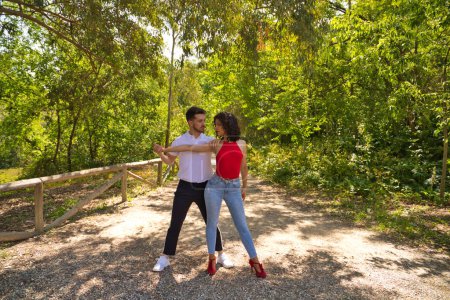 Foto de Handsome young man and woman dancing bachata and salsa in the park. The couple dance passionately surrounded by greenery. Dancing concept. - Imagen libre de derechos