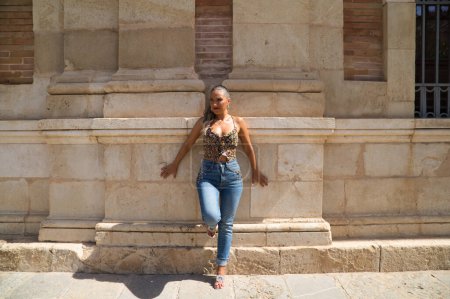 Téléchargez les photos : Belle jeune femme blonde espagnole se penche contre le mur d'un vieux bâtiment à Séville. La femme est habillée en jeans. La femme fait du tourisme et visite l'Espagne. - en image libre de droit