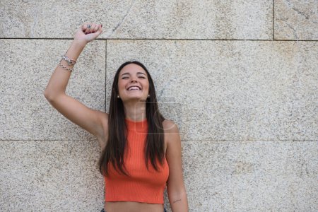 Foto de Beautiful young woman raises her arms with clenched fists celebrating victory and achievements on gray background. - Imagen libre de derechos