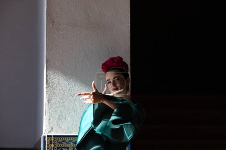Téléchargez les photos : Belle jeune femme en robe à volants verte typique dansant le flamenco sur la place d'Espagne à Séville, en andalousie. Elle fait un geste flamenco avec ses mains regardant la caméra - en image libre de droit