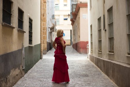 Beautiful blonde mature woman dressed in an elegant dress parading down the street like a model. The woman is happy and enjoying the day