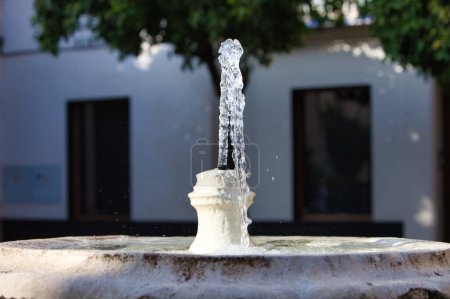 Téléchargez les photos : Ruisseau d'eau cristalline jaillissant de la fontaine de pierre. En arrière-plan maison murale blanche de style méditerranéen en Espagne - en image libre de droit