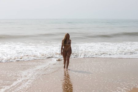 Die schöne junge blonde Frau, die aus dem Meer kommt, spaziert am Strand entlang. Die Frau trägt einen Leoparden-Bikini und genießt ihren Sommerurlaub in Spanien. Reisekonzept
