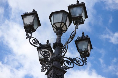 Lampadaire vintage en fer forgé en métal noir avec des détails figuratifs au premier plan contre un ciel bleu par une journée ensoleillée à Séville, Espagne