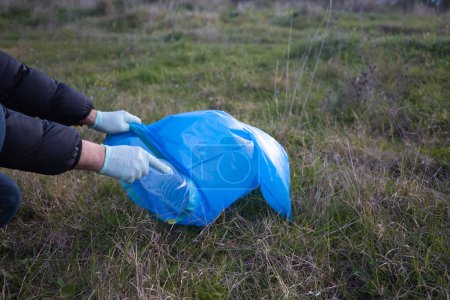Detail von der Hand eines Freiwilligen, der Plastikflaschen aus dem Wald aufhebt und in die Plastiktüte steckt. Konzept für den Tag der Erde und den Weltumwelttag am 5. Juni.