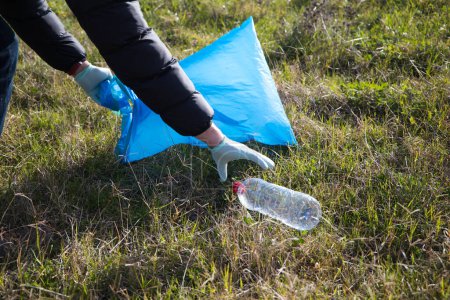 Hand-Detail eines Freiwilligen, der Plastikflaschen aus dem Wald sammelt, um sie in den Recyclingbeutel zu stecken. Konzept für den Tag der Erde und den Weltumwelttag am 5. Juni.