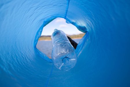 Détail de la main d'un volontaire mettant une bouteille en plastique dans le sac. Photo prise d'en bas. Concept de Journée de la Terre et Journée mondiale de l'environnement 5 juin.