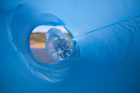 Detail of a volunteer's hand putting a plastic bottle in the bag. Photo taken from below. Concept of Earth Day and World Environment Day June 5.