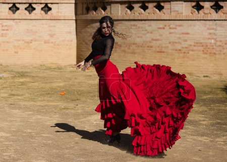 Foto de Hermosa mujer bailando flamenco en Sevilla, España. Lleva un vestido rojo y negro típico de una bailarina de flamenco con mucho arte, se puede ver el movimiento en el aire del vestido de volantes. - Imagen libre de derechos