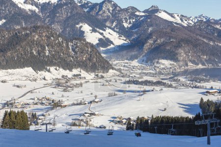 Walchsee Dorf in einem Bergtal an einem sonnigen Wintertag mit einem Skilift im Vordergrund. Österreich.
