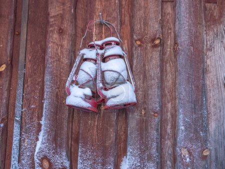 Foto de Dos viejas lámparas de queroseno cubiertas de nieve cuelgan de una pared de madera. Decoración de invierno. - Imagen libre de derechos