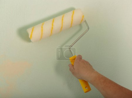 Téléchargez les photos : Woman using paint roller with a yellow handle. Building, renovation and construction work. Tools for painting walls. Human Hand holding new roller brush. A men hand hold paint roller and painting wall - en image libre de droit