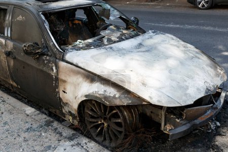 Photo for Remains of a burned car. Burned out car on roadside down in the middle of the street. Burnt new car, vandalism, mafia. Windows shattered from the explosion.  Setting fire to cars of a terrorist attack - Royalty Free Image
