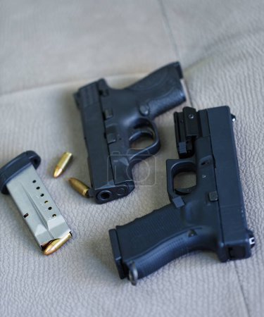 Two pistols with magazine loaded with 9mm bullets on a grey background. Set of black handguns and magazine with 9mm bullets in front. Camera is focused on the magazines and muzzle of the pistol barrel