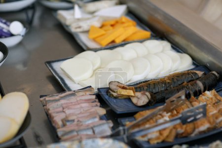 a variety of cheeses and fish arranged on trays. The foreground shows sliced meats, while the middle ground focuses on neatly arranged slices of white soft cheese and smoked herring,salted fish fillet