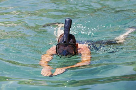 Photo for Caucasian man snorkeling in clear waters with black goggles and a snorkel, arms are extended forward as they swim. Male wearing with the  black snorkel full face mask diving above the water in sea - Royalty Free Image
