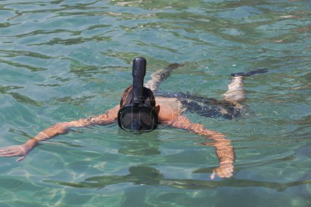 Photo for Man snorkeling in clear sea water. The individual is wearing a black mask and snorkel. Only the arms and top of the head of the person are visible the rest of the body is submerged. Mask snorkeling - Royalty Free Image