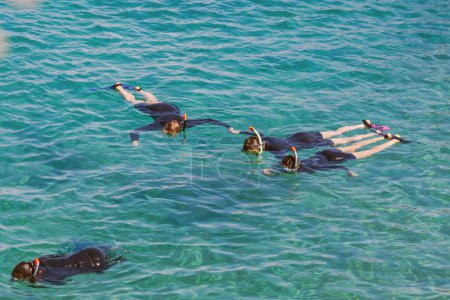 Schnorcheln im türkisfarbenen Wasser. Alle sind mit schwarzen Neoprenanzügen und unverzichtbarer Schnorchelausrüstung wie Masken und Schnorchel ausgestattet. Sie treiben auf der Meeresoberfläche. Abenteuer unter Wasser