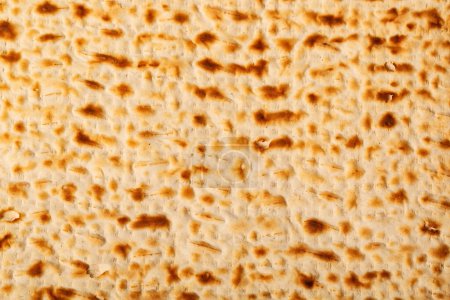 Close up view of matzah, an unleavened flatbread significant in Jewish Passover. The surface is perforated and browned, highlighting its baked texture. Passover matzo, Jewish unleavened matzo bread.