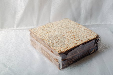 Boîte couverte de matsa, un pain plat sans levain significatif dans la Pâque juive sur une nappe blanche. La surface est perforée et dorée, soulignant sa texture cuite au four. Pain Matzo, sans levain