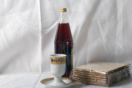 Eine Packung Matza, eine Kiddusch-Tasse und eine Flasche Traubensaft vor dem Hintergrund weißer Spitzenvorhänge werden typischerweise während der Pessach-Feier konsumiert. Jüdische Grußkarte zum Pessachfest