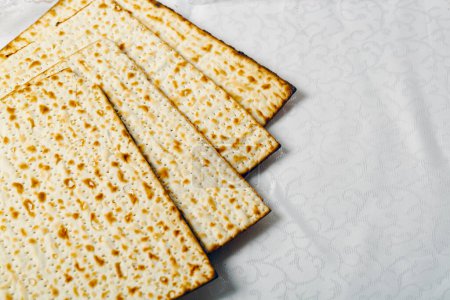 Matzo, an unleavened flatbread integral to Jewish Passover on a textured white surface. The matzo, light and crisp with golden brown spots from baking, symbolizes the Jews hasty exodus from Egypt.