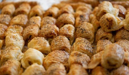 Photo for Freshly baked golden brown burekas with their flaky texture is a type of Jewish pastry. Bourekas are pies that are usually filled with cheese, potatoes, or other fillings, sprinkled with sesame seeds - Royalty Free Image