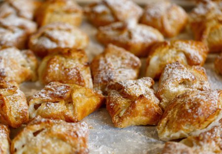 Photo for Freshly baked pastries, golden brown in color on a baking sheet. They are generously sprinkled with powdered sugar giving them a sweet appearance. The texture of the pastries looks flaky and crispy. - Royalty Free Image