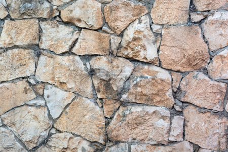 Eine Wand aus Steinen in verschiedenen Größen und Farben, von hellbeige bis dunkelbraun. Die Steine haben eine unregelmäßige Form und Größe und sind ohne sichtbaren Zement oder Mörtel eng miteinander verbunden.