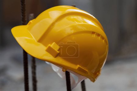 Leuchtend gelber Schutzhelm, der an einer senkrecht stehenden Metallstange hängt. Der Helm symbolisiert Sicherheit und Vorsorge. Konstruktionsstruktur im Freien, Hintergrund verschwimmt und lenkt die Aufmerksamkeit auf den Helm