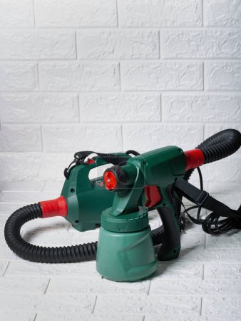 Green and red electric paint sprayer on white brick background in daylight. An electric paint sprayer with green and red parts is placed on brick surface showcasing its design and functionality