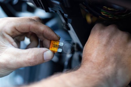 Hands working on a car, specifically handling an orange automotive fuse. Protecting the cars electrical circuits. Auto repair or electrical safety. Electrical car fuse or breaker. Automotive fuses