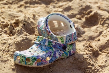 Zapato colorido para niños con un patrón de hojas y formas geométricas abandonadas en una playa de arena. El zapato aparece parcialmente enterrado, día lúdico o la naturaleza transitoria de los momentos de la infancia. chanclas en la arena de verano