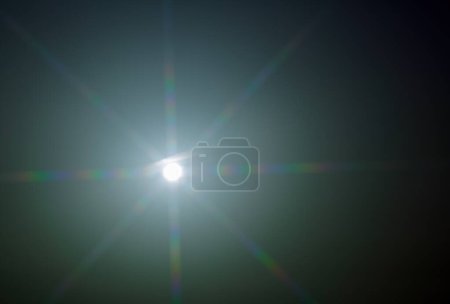 The image depicts a bright sun with rays radiating outward, creating a starburst effect against a gradient sky. The visual pattern illustrates diffraction, where light waves bend around obstacles.