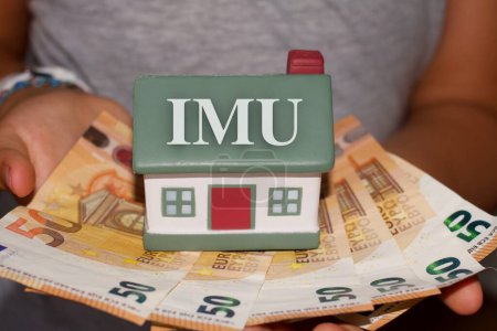Téléchargez les photos : Personne tenant une maison avec billets en euros avec le signe "Imu" impôt italien - en image libre de droit