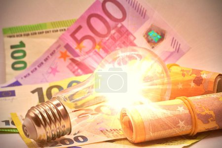 Glühbirne eingeschaltet, Euroscheine herumgereicht. Erhöhung der Strompreise, Energieabhängigkeit, Energiequellen und Energieversorgung.