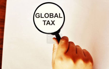 Agrandissement du verre sur la pile d'argent avec le texte "Global Tax". Concept de la nouvelle taxe européenne.