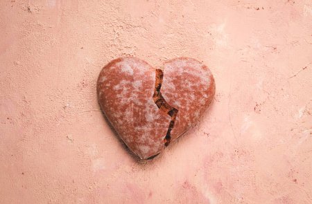 Pan de jengibre de chocolate esmaltado, en forma de corazón, vista superior, un corazón roto, primer plano, sobre fondo beige, sin personas,