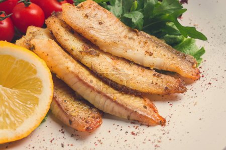 Foto de Fried Tilapia fish fillet, in spices, with cherry and salad, on a white plate, homemade, no people, - Imagen libre de derechos