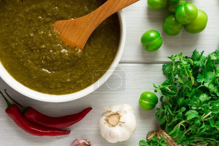 Photo for Tkemali sauce, traditional Georgian cuisine, green cherry plum, with ingredients for sauce, cilantro, mint, hot pepper, garlic, on a white wooden table, close-up, rustic, food background, no people - Royalty Free Image