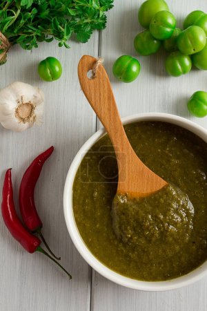 Photo for Tkemali sauce, traditional Georgian cuisine, green cherry plum, with ingredients for sauce, cilantro, mint, hot pepper, garlic, on a white wooden table, close-up, rustic, food background, no people, selective focus, sauce, green sauce, tkemali, georg - Royalty Free Image