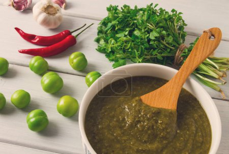 Photo for Tkemali sauce, traditional Georgian cuisine, green cherry plum, with ingredients for sauce, cilantro, mint, hot pepper, garlic, on a white wooden table, close-up, rustic, food background, no people, selective focus, sauce, green sauce, tkemali, georg - Royalty Free Image