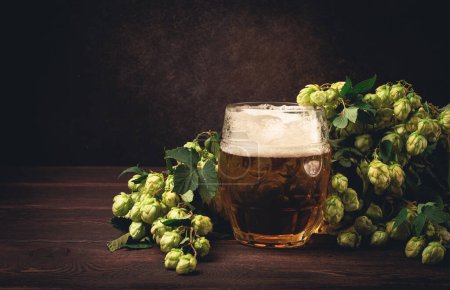 A mug of beer , on a wooden table, with a branch of fresh hops, rustic , no people,