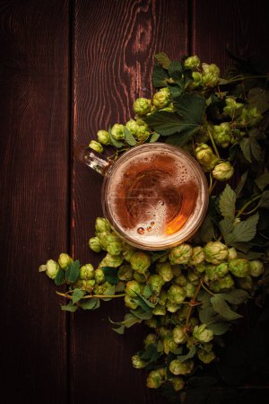 A mug of beer , on a wooden table, with a branch of fresh hops, rustic , no people,