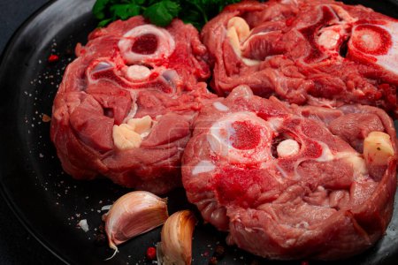 rohes Steak, Kalbshals am Knochen, frisches Fleisch, auf schwarzem Teller, Draufsicht, keine Menschen,