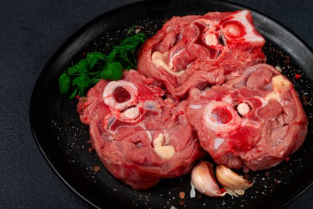 rohes Steak, Kalbshals am Knochen, frisches Fleisch, auf schwarzem Teller, Draufsicht, keine Menschen,