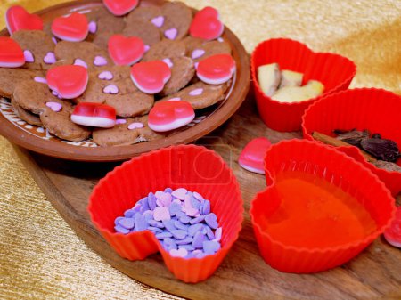 Vegetarische Kekse verschiedener Herzsorten, die mit Tauchgeräten hergestellt werden. Dekoriert mit natürlichen Säften, die mit Agar-Agar verdickt sind. Schokoladenbonbons in Herzform in roten und gemischten Farben. Goldener Hintergrund.