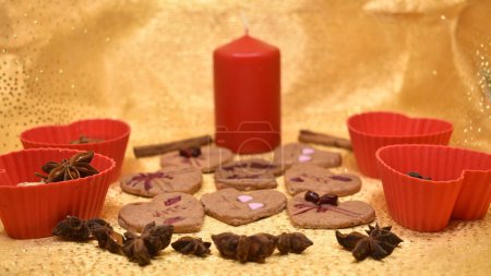 Vegetarian cookies of different types of hearts made using plungers. Decorated with natural juices thickened with agar-agar. Gold background. Red candle