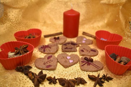 Vegetarian cookies of different types of hearts made using plungers. Decorated with natural juices thickened with agar-agar. Gold background. Red candle